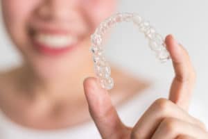 A smiling woman holding invisalign or invisible braces