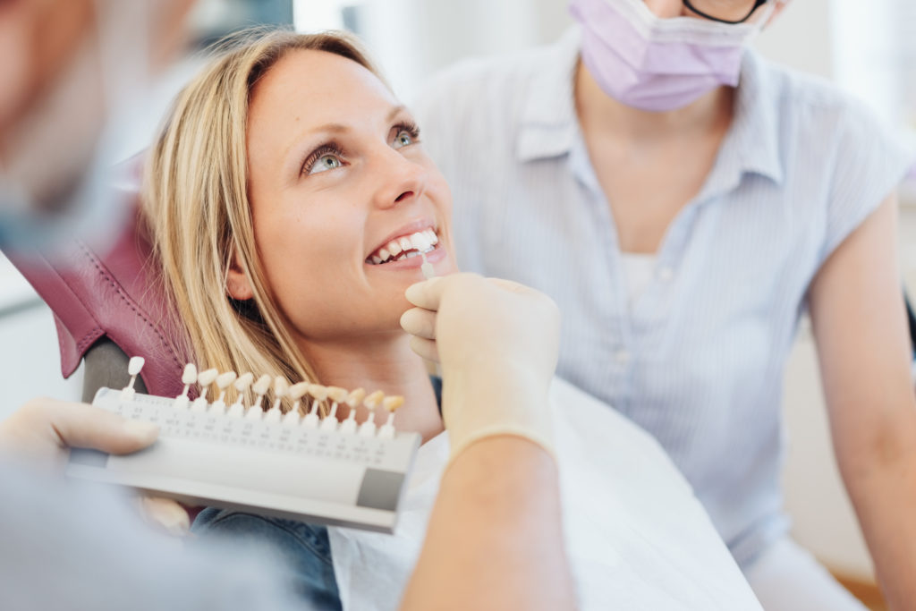 Dentist checking color of porcelain veneer against patient's teeth