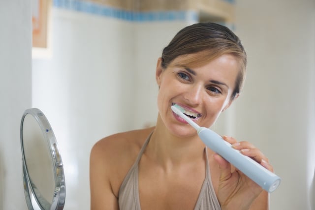 woman brushing teeth with electric toothbrush