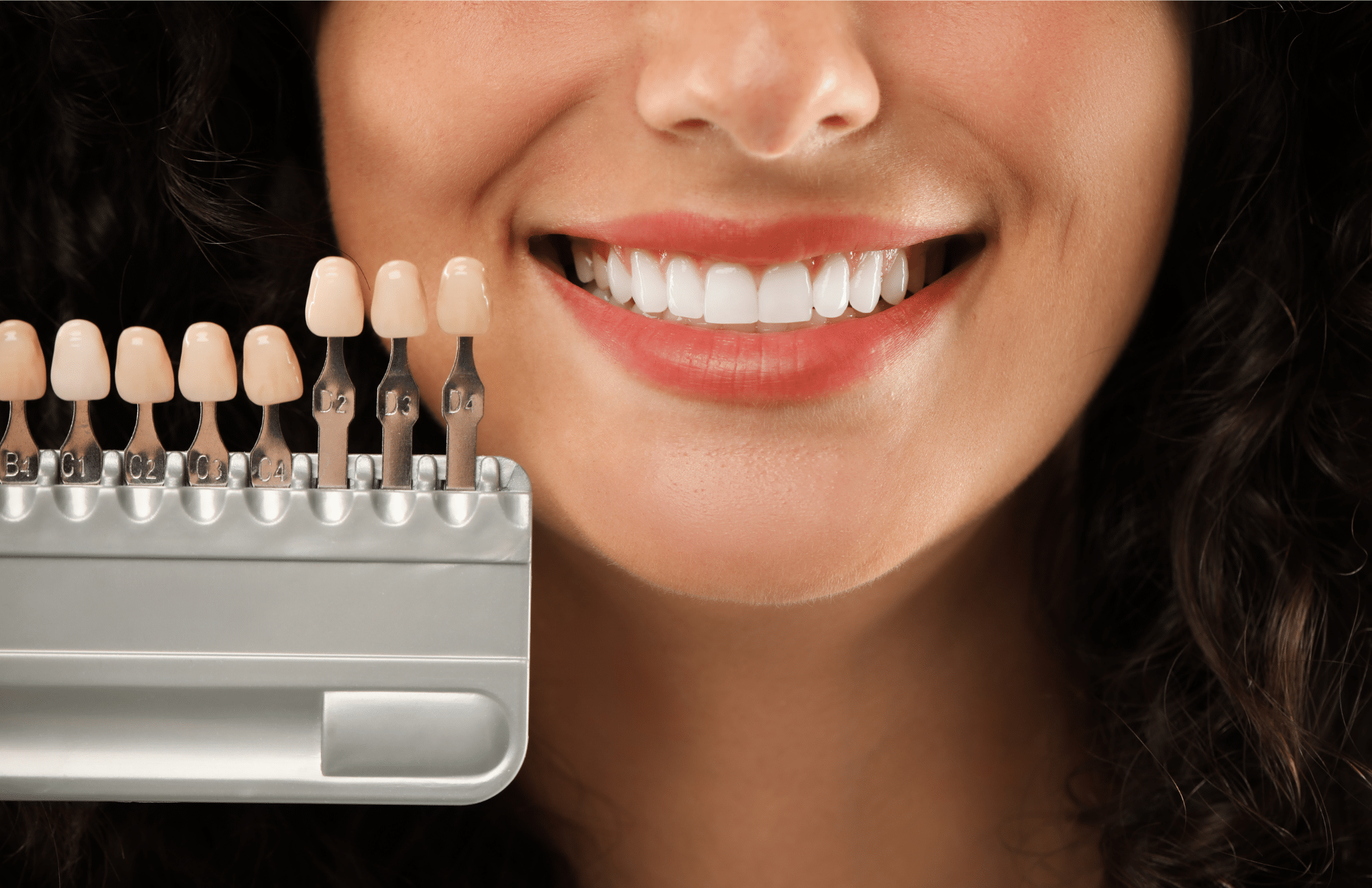 smiling woman holding a sample of porcelain veneers at Pacific Northwest Smiles at Mill Creek